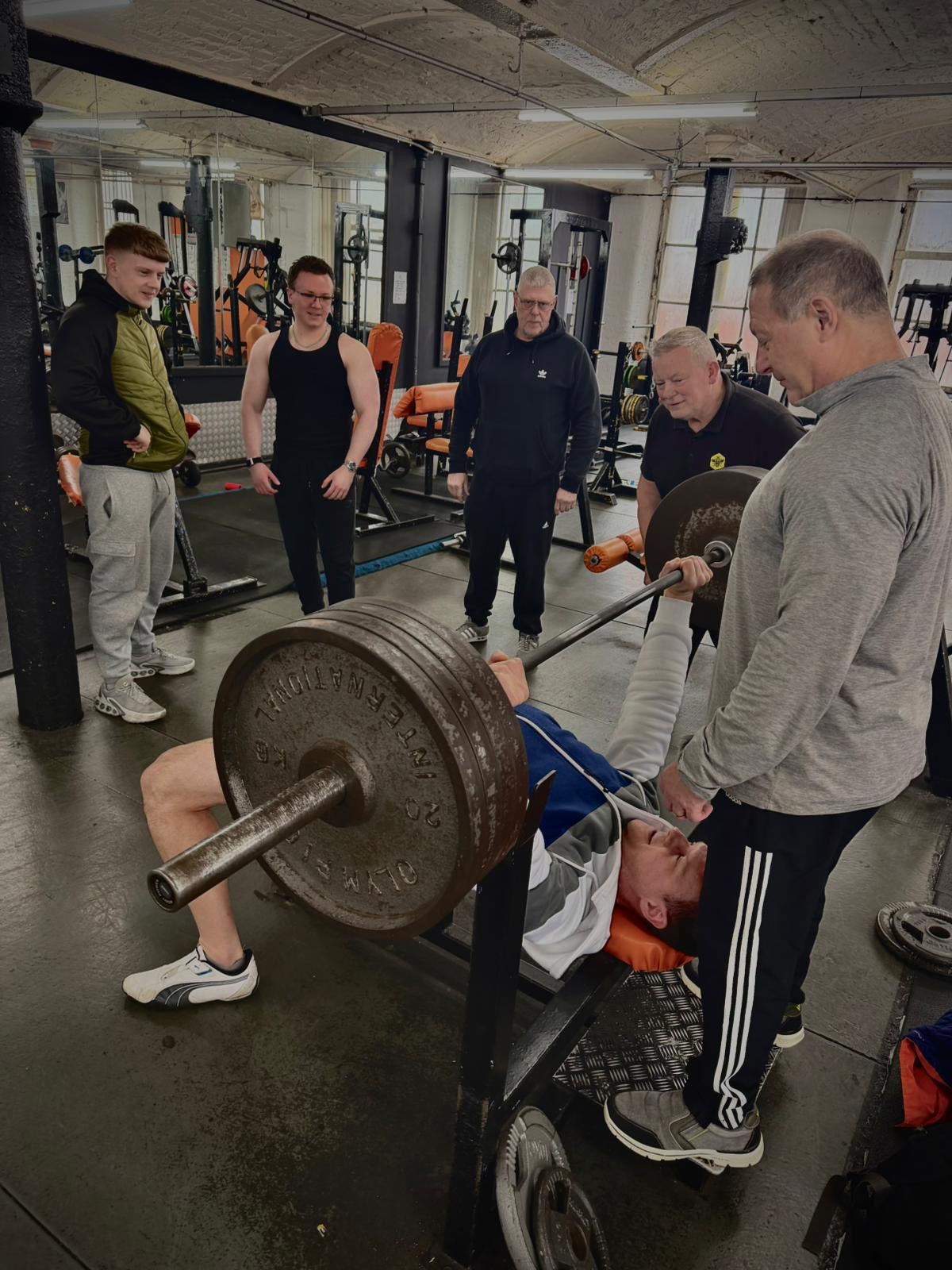 Member bench pressing with spotters and friends watching on